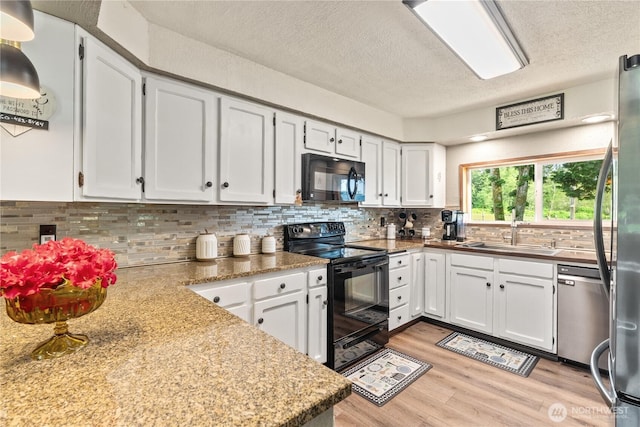 kitchen with a textured ceiling, a sink, white cabinets, black appliances, and light wood finished floors