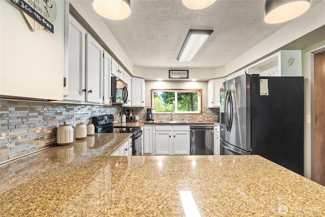 kitchen featuring a sink, a textured ceiling, stainless steel appliances, white cabinetry, and decorative backsplash