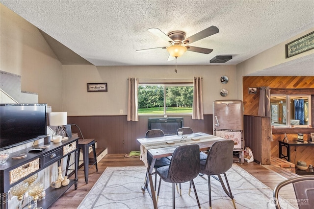 dining room featuring wooden walls, a textured ceiling, ceiling fan, and a wainscoted wall