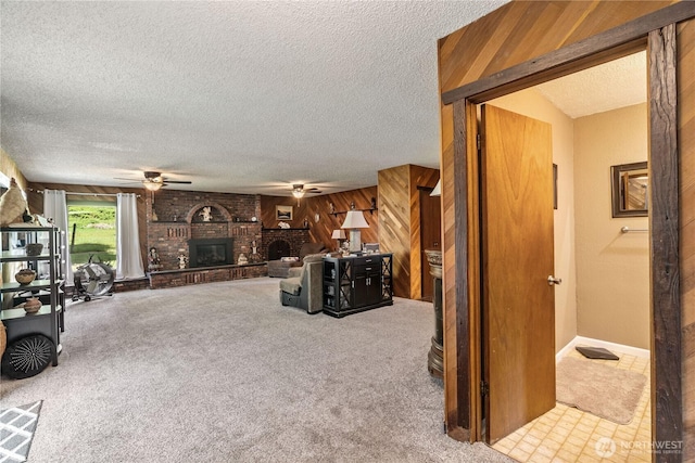 carpeted living area featuring a ceiling fan, a textured ceiling, a brick fireplace, and wooden walls