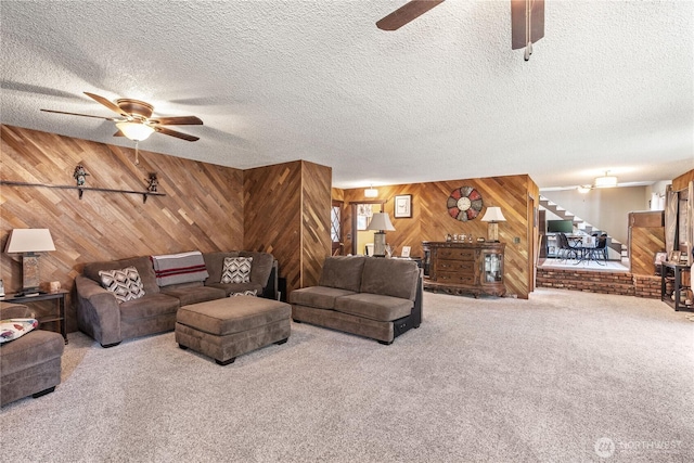 carpeted living area featuring a textured ceiling, ceiling fan, stairs, and wooden walls