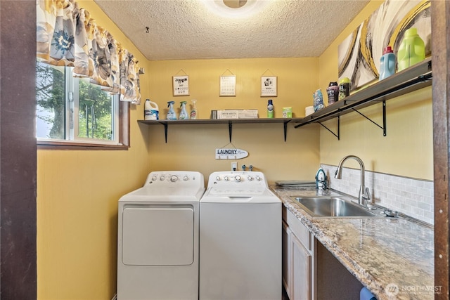 clothes washing area featuring a sink, a textured ceiling, cabinet space, and washer and clothes dryer