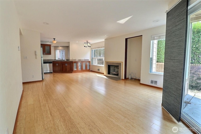 unfurnished living room featuring visible vents, a sink, light wood-style floors, baseboards, and a fireplace with flush hearth