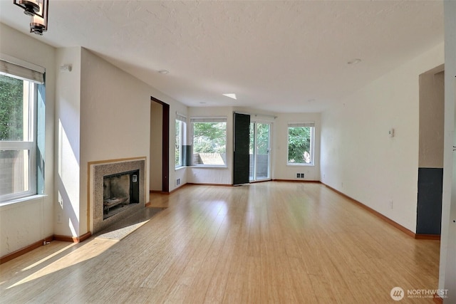 unfurnished living room with visible vents, baseboards, a fireplace with flush hearth, and light wood finished floors