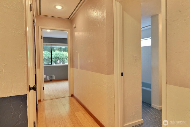 corridor with a textured wall, wood finished floors, and visible vents