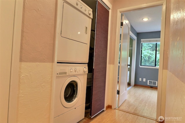 laundry area with visible vents, a textured wall, stacked washer / dryer, light wood-style floors, and baseboards