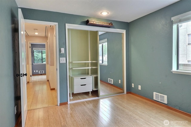 unfurnished bedroom featuring baseboards, a closet, wood finished floors, and visible vents