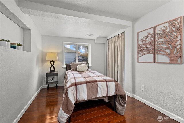 bedroom featuring baseboards, a textured wall, wood finished floors, and visible vents