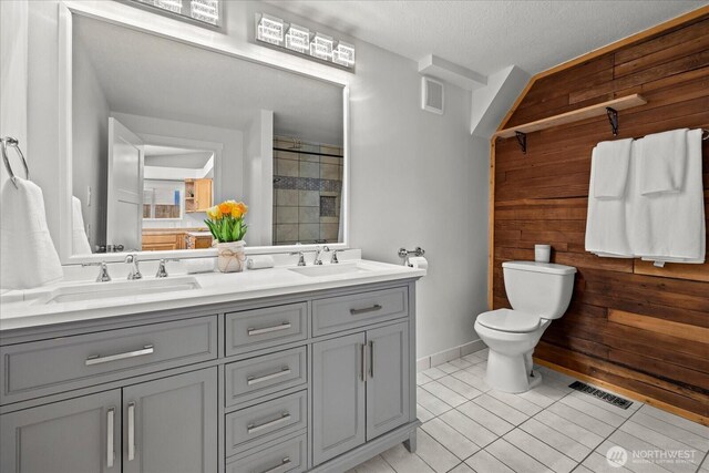 bathroom featuring a sink, toilet, wooden walls, and visible vents