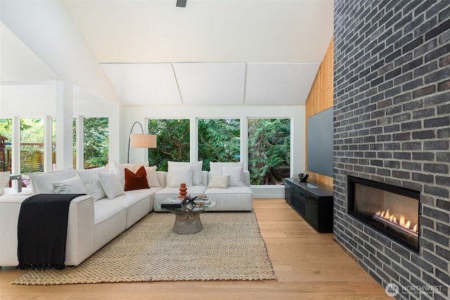 living area with light wood-type flooring, plenty of natural light, a fireplace, and high vaulted ceiling