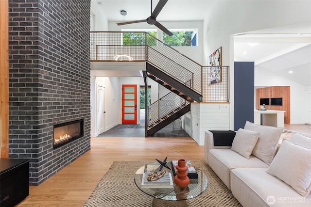 living room with high vaulted ceiling, a large fireplace, a ceiling fan, wood finished floors, and stairway