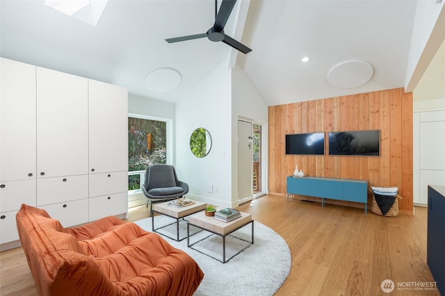 living area featuring wood walls, baseboards, ceiling fan, high vaulted ceiling, and light wood finished floors