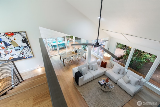 living area with baseboards, a high ceiling, ceiling fan, and wood finished floors