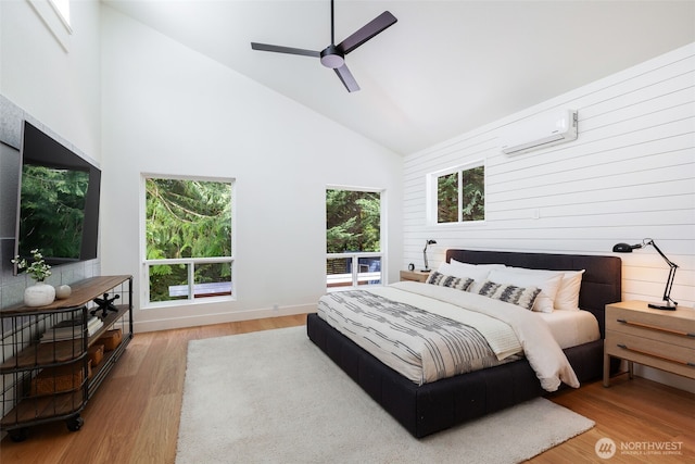 bedroom featuring ceiling fan, a wall unit AC, wood finished floors, high vaulted ceiling, and baseboards