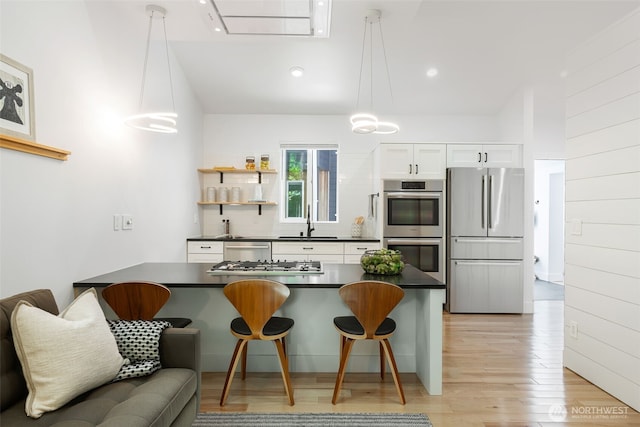 kitchen with dark countertops, a kitchen bar, white cabinets, a sink, and stainless steel appliances