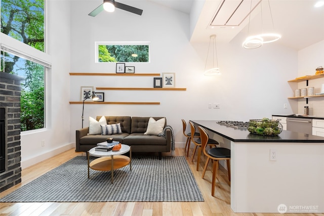 living area with high vaulted ceiling, ceiling fan, a wealth of natural light, and light wood-style floors