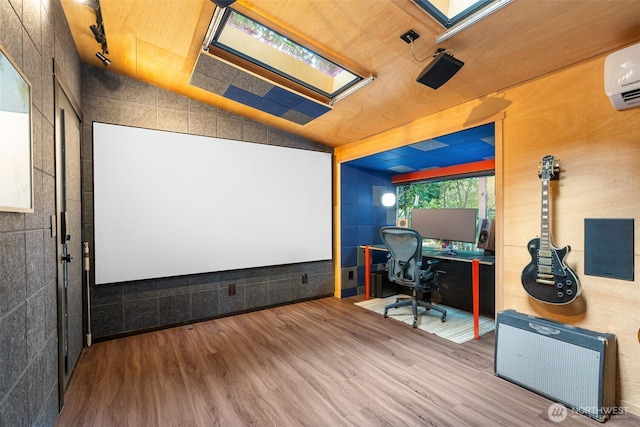 home theater room featuring vaulted ceiling with skylight, track lighting, a wall unit AC, and wood finished floors