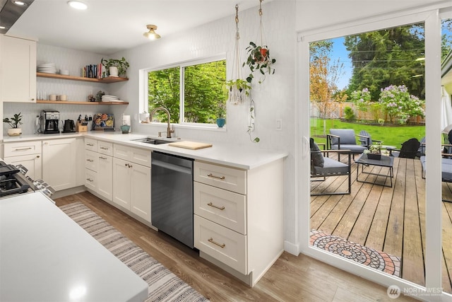 kitchen featuring stainless steel dishwasher, light countertops, white cabinetry, a sink, and light wood finished floors