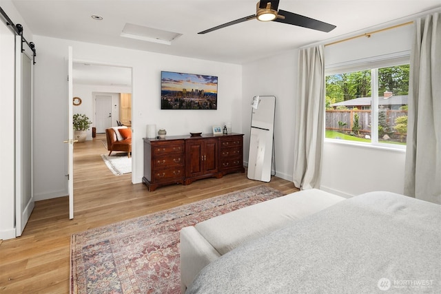 bedroom with a ceiling fan, attic access, light wood-type flooring, a barn door, and baseboards