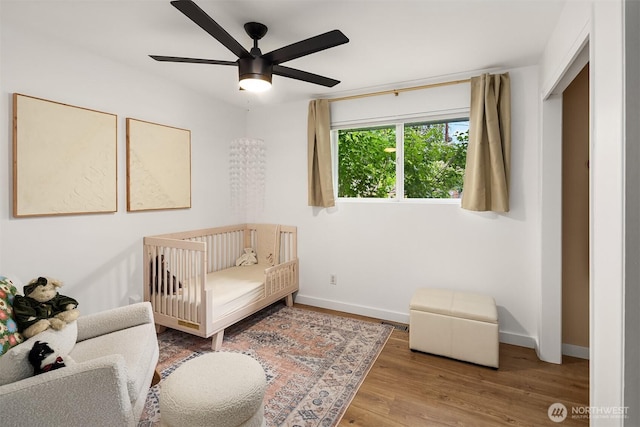 bedroom featuring a ceiling fan, baseboards, a crib, and wood finished floors