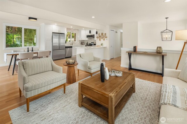 living room with recessed lighting, light wood-style flooring, baseboards, and a notable chandelier