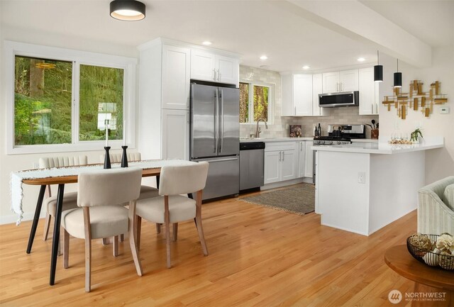 kitchen featuring decorative backsplash, appliances with stainless steel finishes, light wood finished floors, a peninsula, and white cabinetry