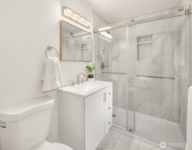 bathroom featuring toilet, a marble finish shower, marble finish floor, and vanity