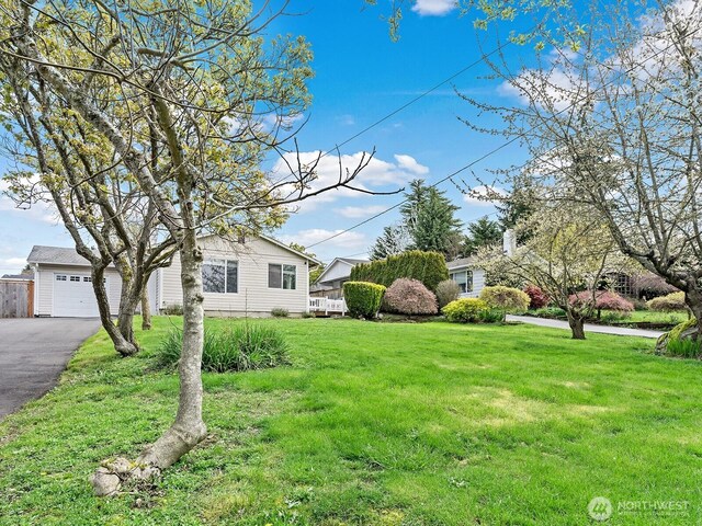 view of property hidden behind natural elements with aphalt driveway, a front yard, and a garage