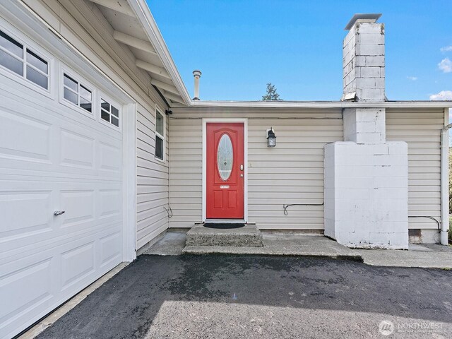 view of exterior entry with an attached garage and a chimney