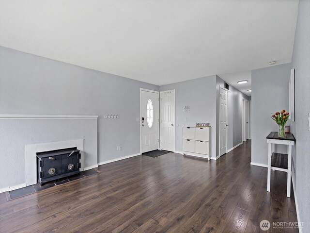unfurnished living room with baseboards, a wood stove, wood finished floors, and visible vents