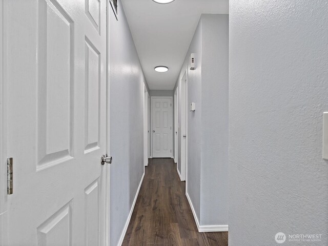 hallway with a textured wall, baseboards, and dark wood-style floors