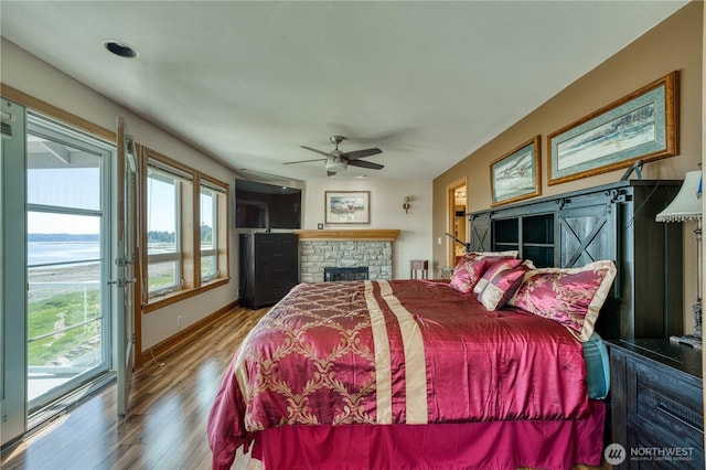 135 NE Boad Haven Rd, Belfair, WA 98528 - bedroom with wood finished floors, access to outside, baseboards, ceiling fan, and a stone fireplace