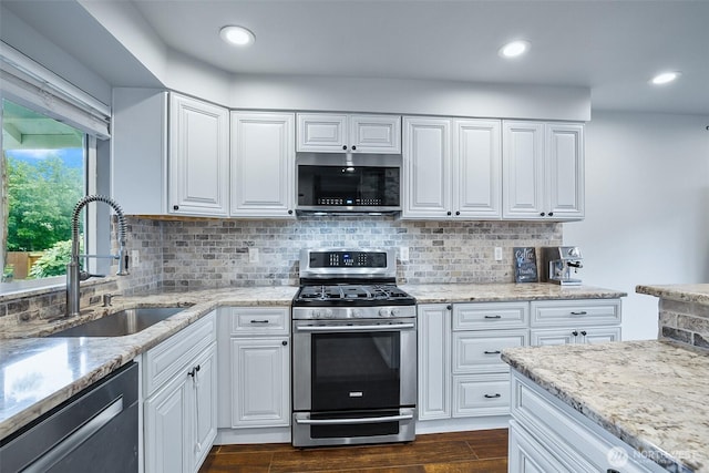 kitchen with appliances with stainless steel finishes, a sink, light stone counters, decorative backsplash, and recessed lighting