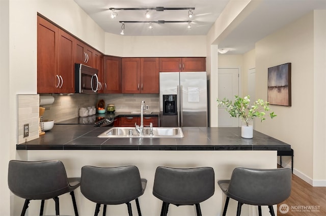 kitchen featuring a peninsula, a kitchen breakfast bar, tasteful backsplash, a sink, and appliances with stainless steel finishes