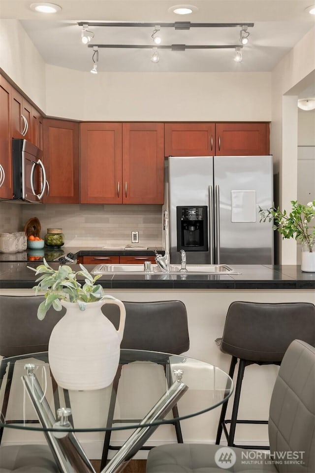 kitchen featuring rail lighting, appliances with stainless steel finishes, a breakfast bar area, and dark countertops