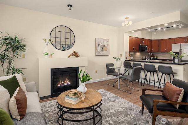 living area featuring baseboards, a glass covered fireplace, and light wood finished floors