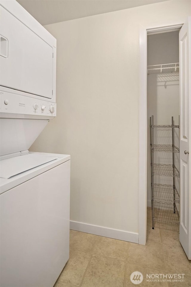 washroom featuring stacked washer and dryer, baseboards, light tile patterned floors, and laundry area