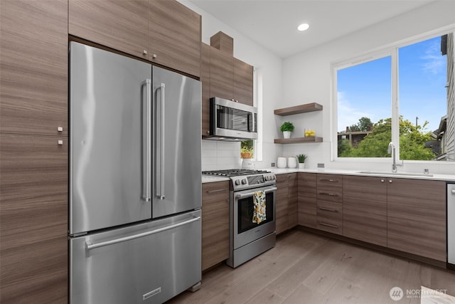 kitchen featuring decorative backsplash, modern cabinets, a sink, light wood-style floors, and stainless steel appliances