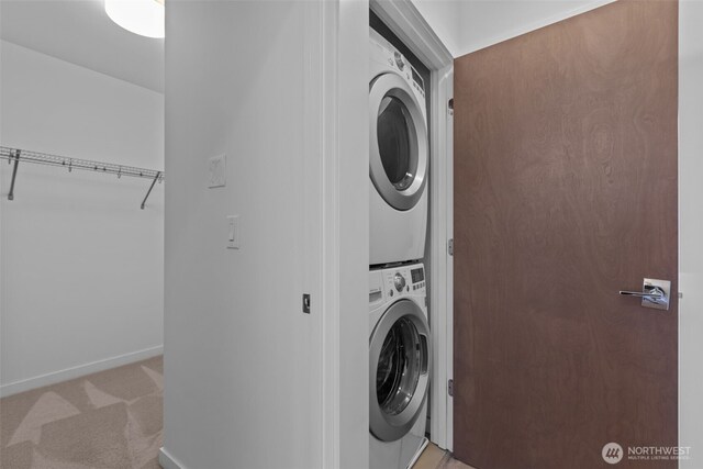 clothes washing area with baseboards, laundry area, stacked washing maching and dryer, and light colored carpet