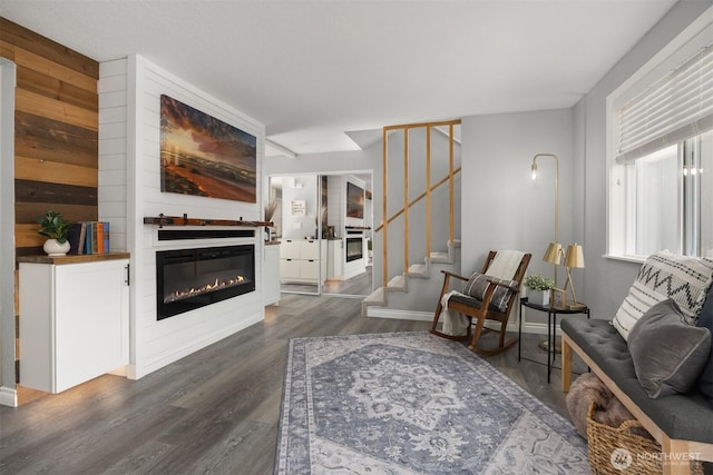 living area featuring dark wood-style floors, stairs, and a glass covered fireplace