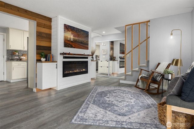 living room featuring dark wood-type flooring, a glass covered fireplace, stairs, recessed lighting, and baseboards