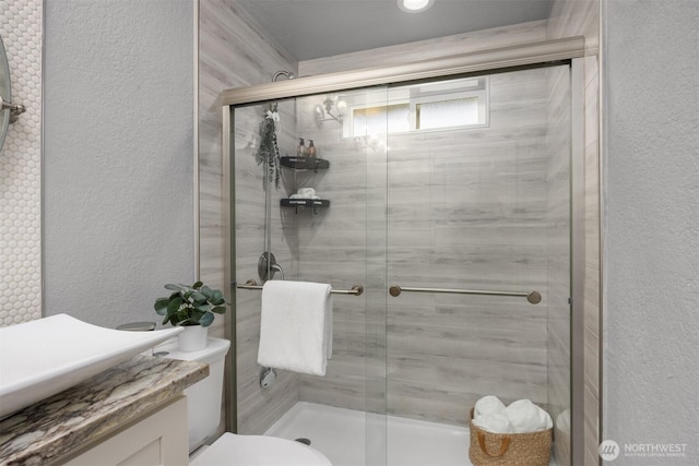 full bathroom with a textured wall, a shower stall, vanity, and toilet