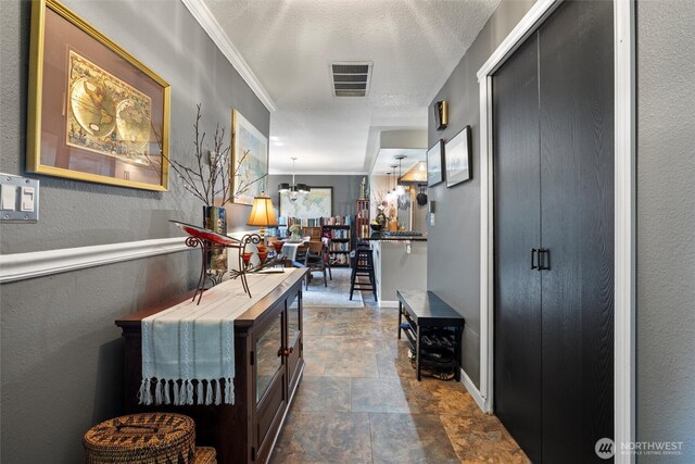 corridor with a textured ceiling, a chandelier, stone finish floor, baseboards, and visible vents