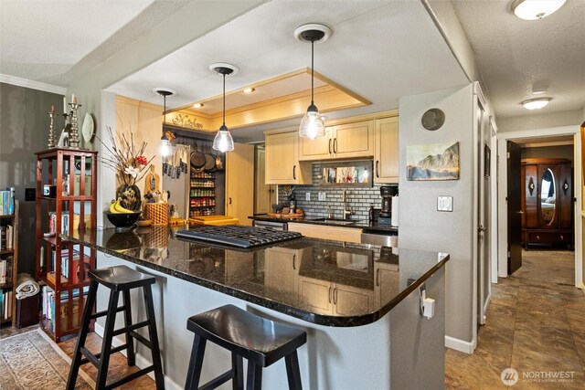 kitchen featuring backsplash, a kitchen bar, gas stovetop, a sink, and light brown cabinets