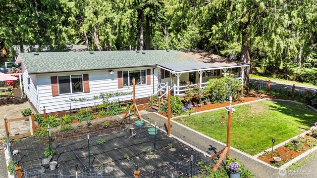 ranch-style house featuring a porch, roof with shingles, a front yard, a vegetable garden, and fence