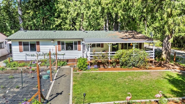 ranch-style home with a front lawn, roof with shingles, covered porch, and a vegetable garden