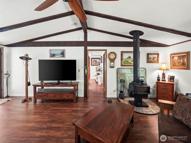 living area with a ceiling fan, a wood stove, wood finished floors, baseboards, and lofted ceiling with beams