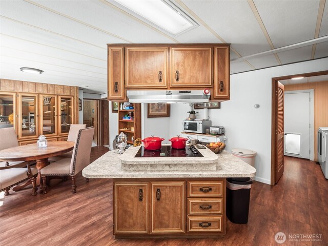 kitchen with brown cabinets, black electric cooktop, stainless steel microwave, separate washer and dryer, and under cabinet range hood