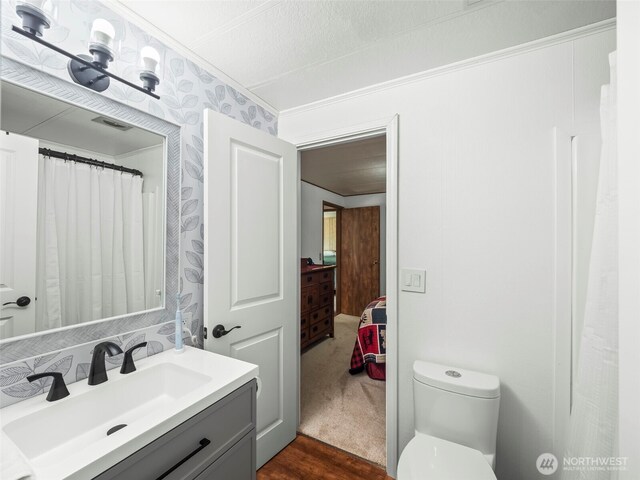bathroom featuring vanity, toilet, wood finished floors, visible vents, and ornamental molding