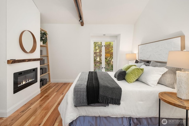 bedroom with baseboards, a glass covered fireplace, and wood finished floors